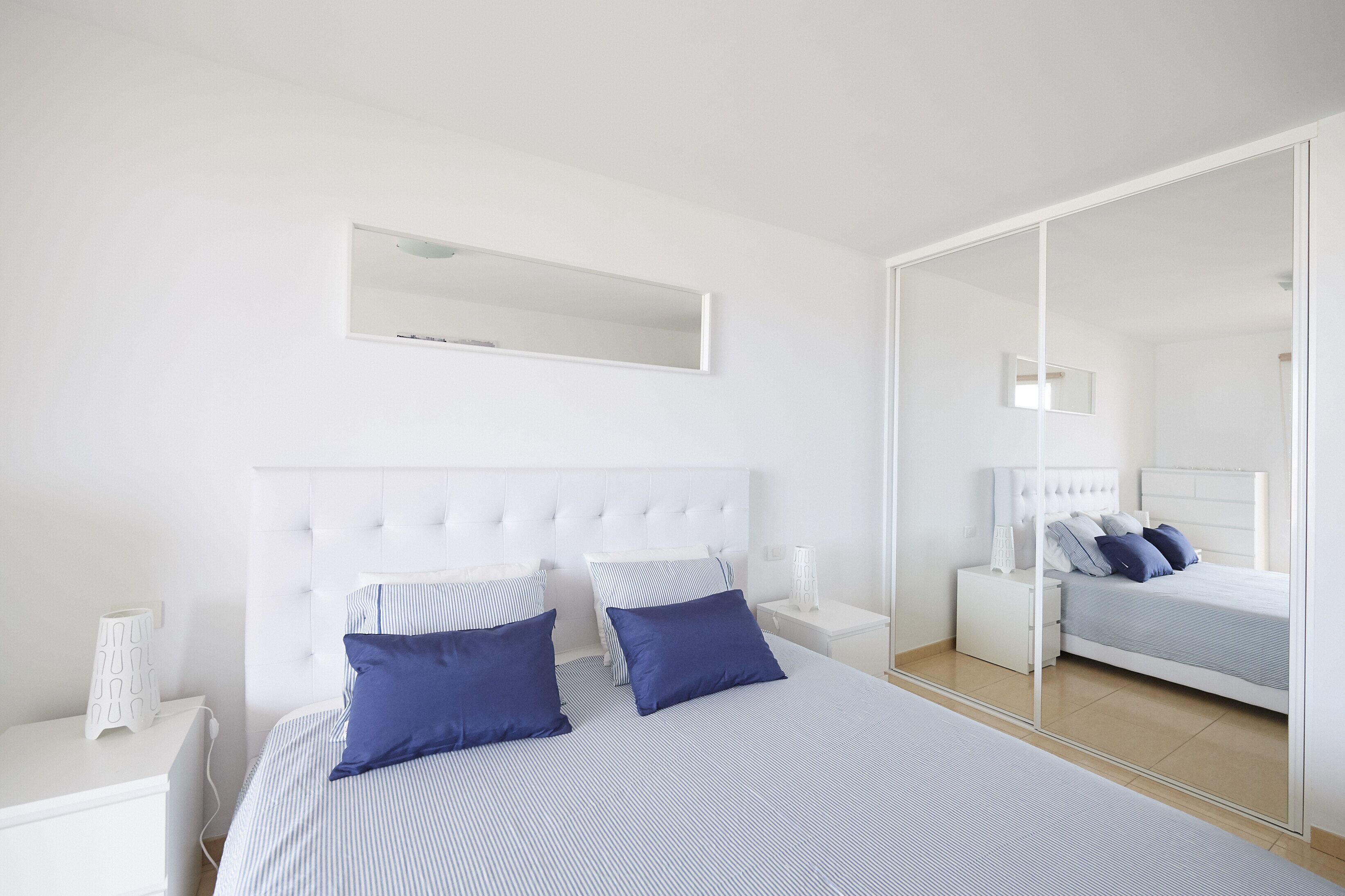 Quarto com cama grande, mesa de cabeceira, espelho e guarda-roupa.