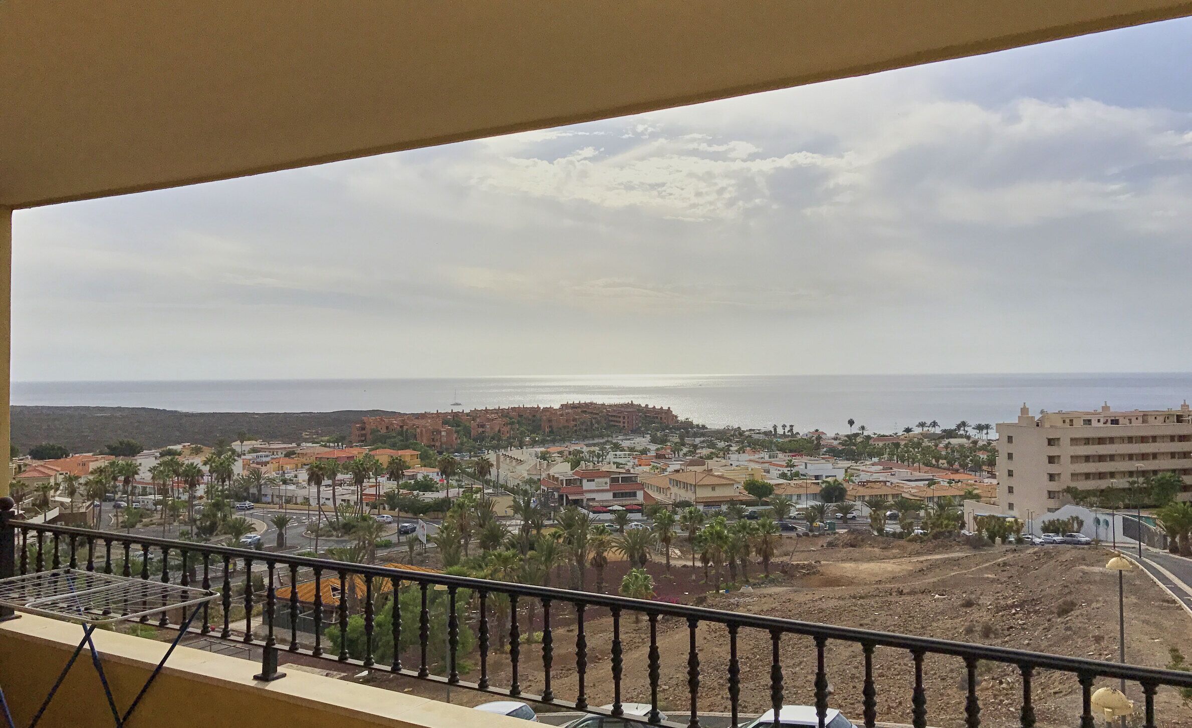 A balcony with a view of a coastal town, featuring buildings, palm trees, and a clear sky.