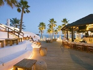A wooden deck with outdoor seating, palm trees, and a beach view. - Lovely 2 bed  Ground Floor Apartment next to 2 Pools set in beautiful gardens. (Marbella)
