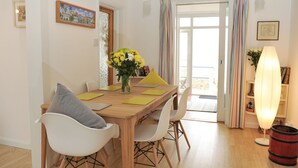 Un coin repas avec une table en bois, des chaises blanches et un vase rempli de fleurs jaunes.