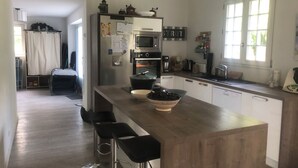 Eine moderne Küche mit Kochinsel, Barhocker, Kühlschrank, Backofen, Mikrowelle und einem Fenster mit Tageslicht.