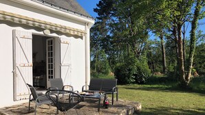 Ein weißes Gebäude mit überdachter Terrasse, ausgestattet mit zwei schwarzen Metallstühlen und einer Bank.