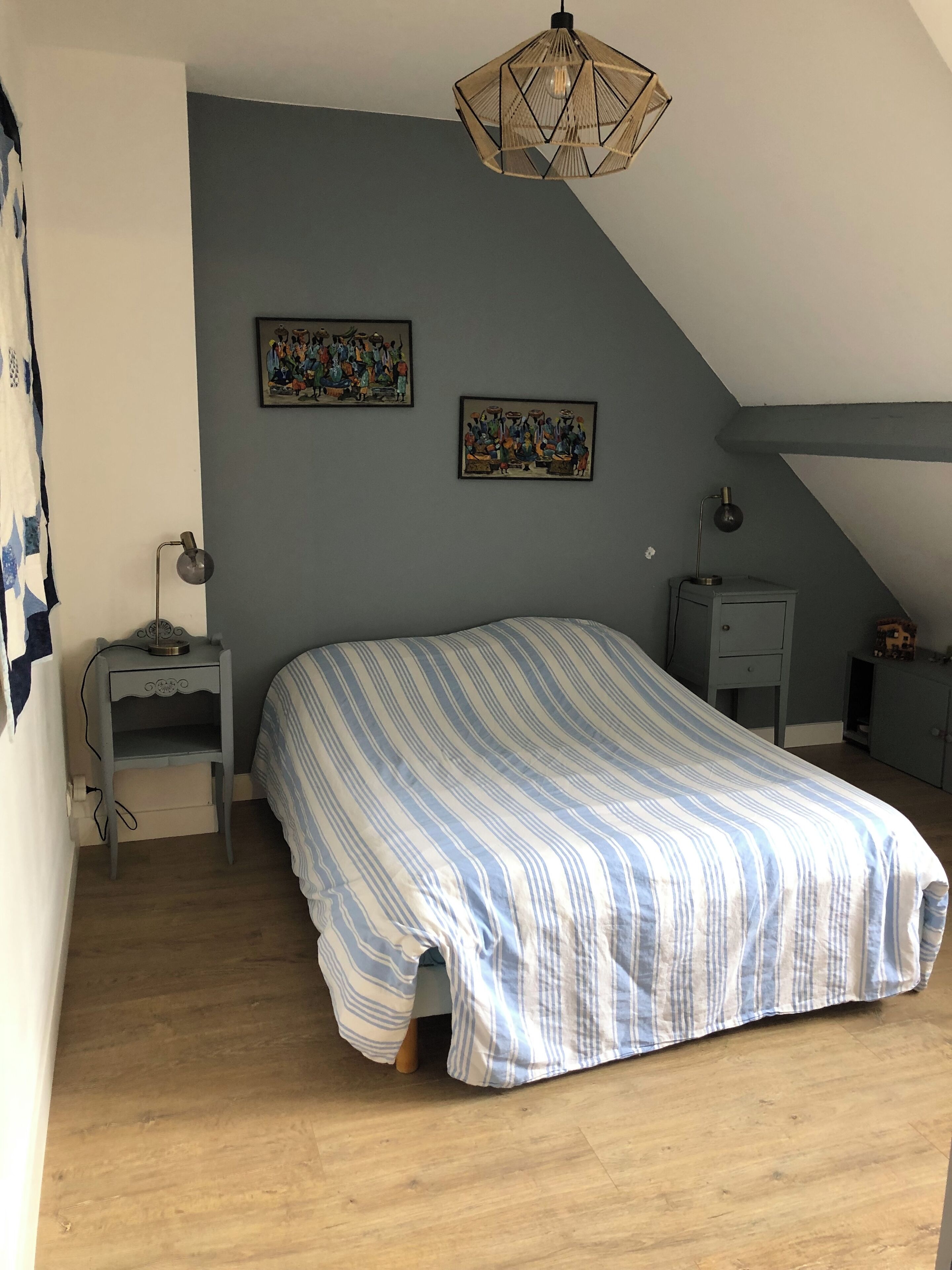 Une chambre à coucher comprenant un lit, une table de chevet, un bureau et deux tableaux accrochés au mur.