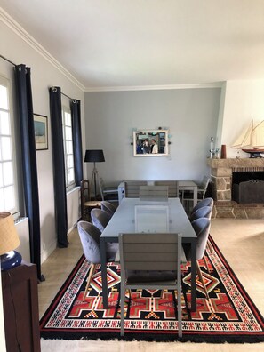 Un'area pranzo con tavolo e sedie, un tappeto decorativo, un caminetto e una finestra con tende.