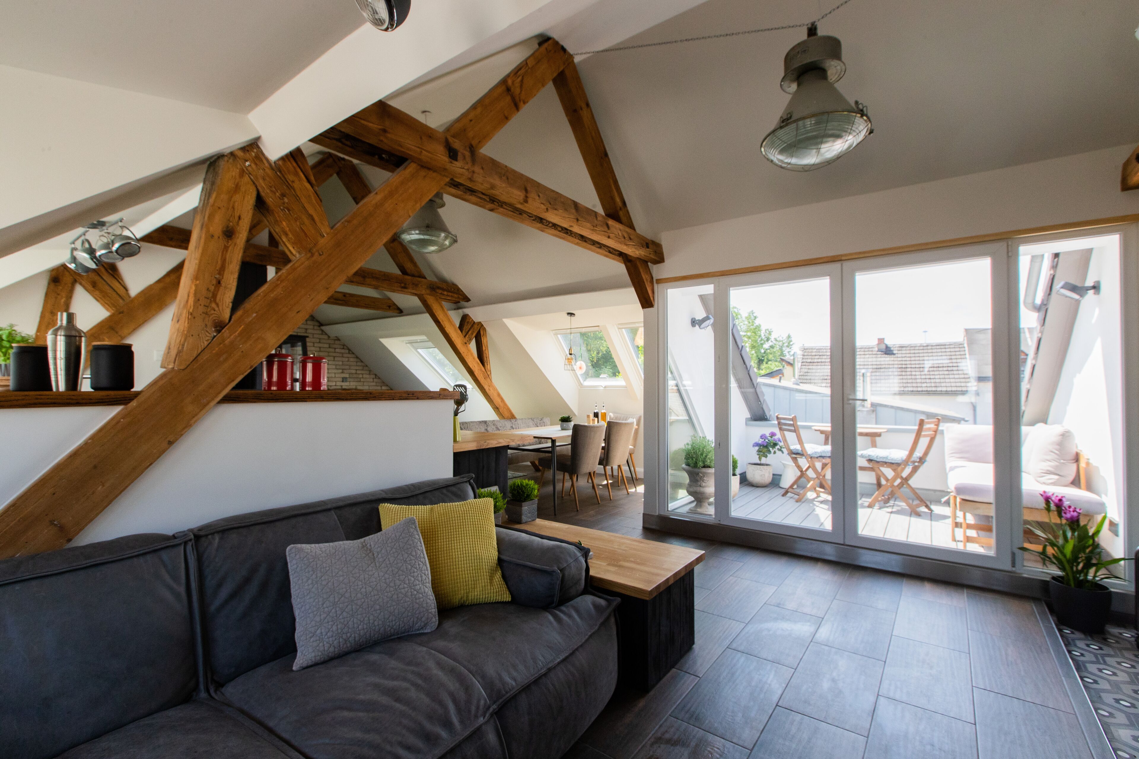 Ein modernes Wohnzimmer mit grauem Sofa, Holzbalken, einem Holztisch und einer großen Schiebeglas-Tür, die auf eine Außenpatio führt.