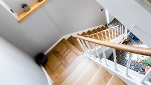 Un escalier en bois avec des rampes blanches, une petite étagère ornée de plantes et un sol à motifs.