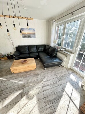 A modern living room with a black leather sectional sofa, a wooden coffee table, and a large window providing natural light.