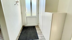 A narrow hallway with a black doormat, a white door with frosted glass panels, and a white wall with a simple light fixture.