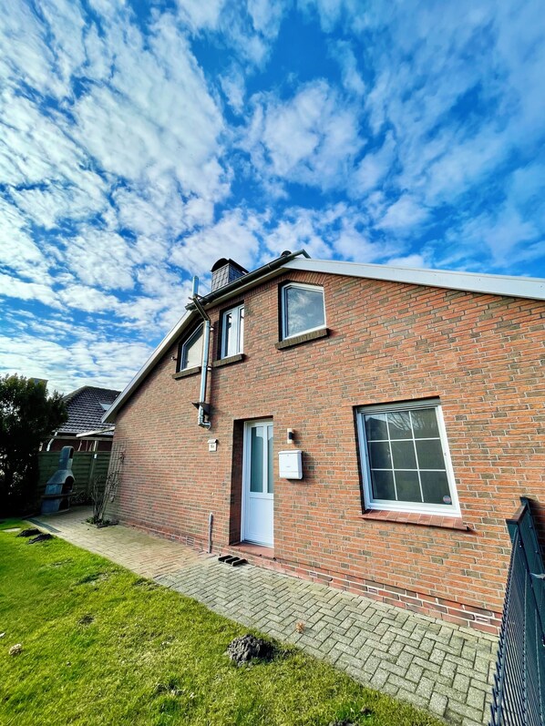 A brick house with a white door, two windows, and a chimney.