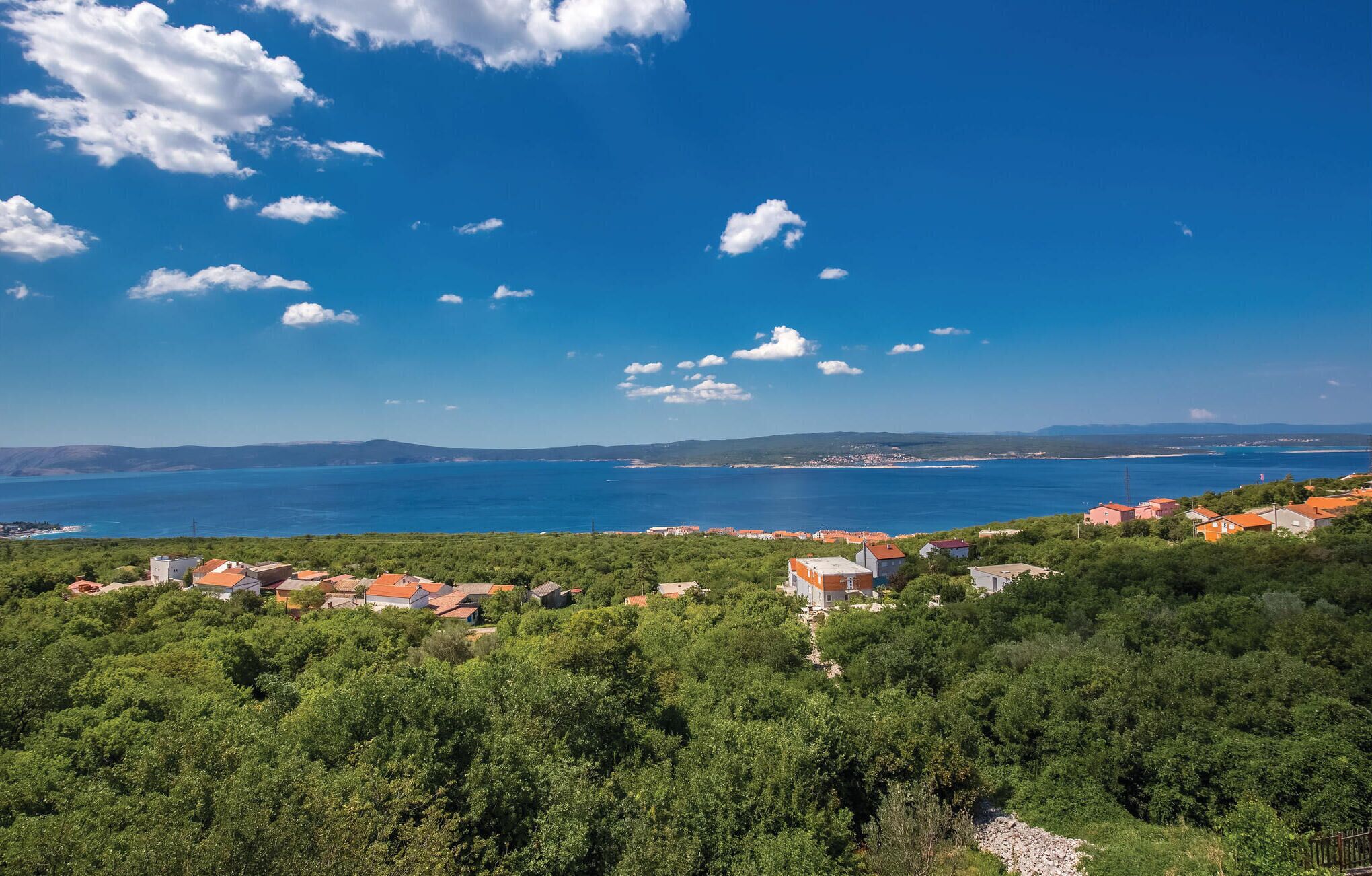 Un pueblo costero con casas rodeado de vegetación, con vistas a una gran extensión de agua y colinas distantes.