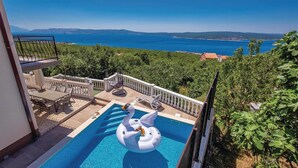 Ein Pool mit einer Schwan-Luftmatratze, Gartenmöbeln und Blick auf das Meer und die Hügel.
