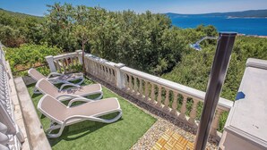 Ein Balkon mit weißen Liegestühlen, einer Holzterrasse und Blick aufs Meer.
