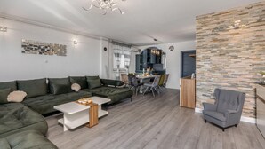 Ein modernes Wohnzimmer mit einer Eckcouch, einem Esstisch und einem grauen Sessel.