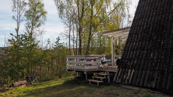 A wooden deck with outdoor seating and a pergola, surrounded by trees and a large tree trunk. - Cozy cottage in the Palatinate Forest - in the southern Wasgau (Gossersweiler-Stein)