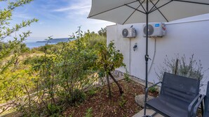 An outdoor seating area with a table and chair, a large umbrella, and air conditioning units on a white wall.