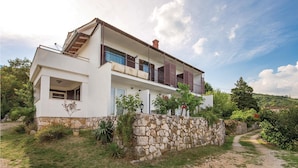 A two-story house with a stone wall foundation, a balcony with wooden shutters, and a clear sky.