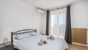 A bedroom with a bed, a nightstand, an air conditioning unit, a window with curtains, and a radiator.