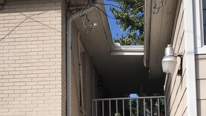 Ein Wohngebäude mit Ziegelaußenwand, einem kleinen Balkon mit weißer Brüstung und einer sichtbaren Tür zu einem Innenraum.