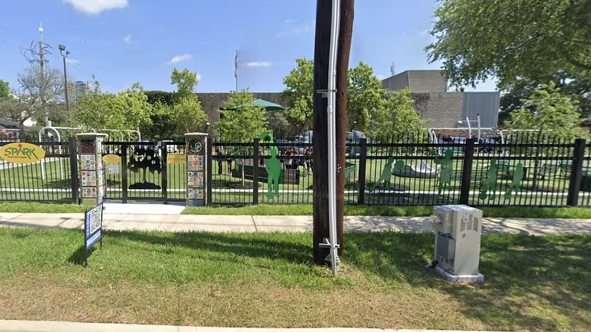 Uma área de parque cercada, com parquinho, lixeira e uma placa com 'SPARK'.