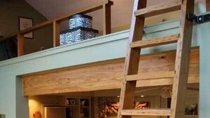 Una habitación tipo loft con una escalera de madera, un televisor, una lámpara y una estantería.