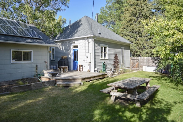 A house with a covered patio, a wooden deck, and a backyard with a picnic table.