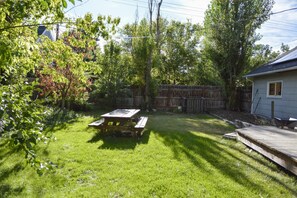 Un jardin avec une table de pique-nique en bois, une terrasse en bois et une clôture en bois.