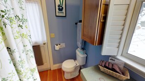 Une salle de bain avec des toilettes, un panier rempli de serviettes, un panneau indiquant comment utiliser les lingettes nettoyantes et une affiche encadrée accrochée au mur.