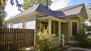 Ein eingeschossiges Haus mit Veranda, Holzpforte und kleinem Garten.