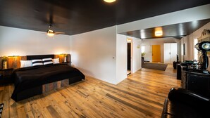 A modern bedroom with a wooden floor, a bed with black bedding, a ceiling fan, and a desk with a record player.