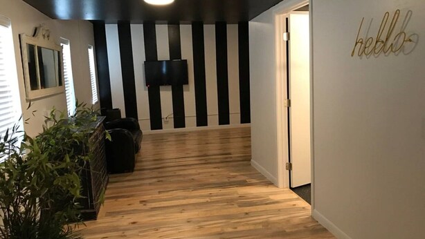 A hallway with black and white striped walls, a flat-screen TV mounted on the wall, a door on the right, and a potted plant on the left.