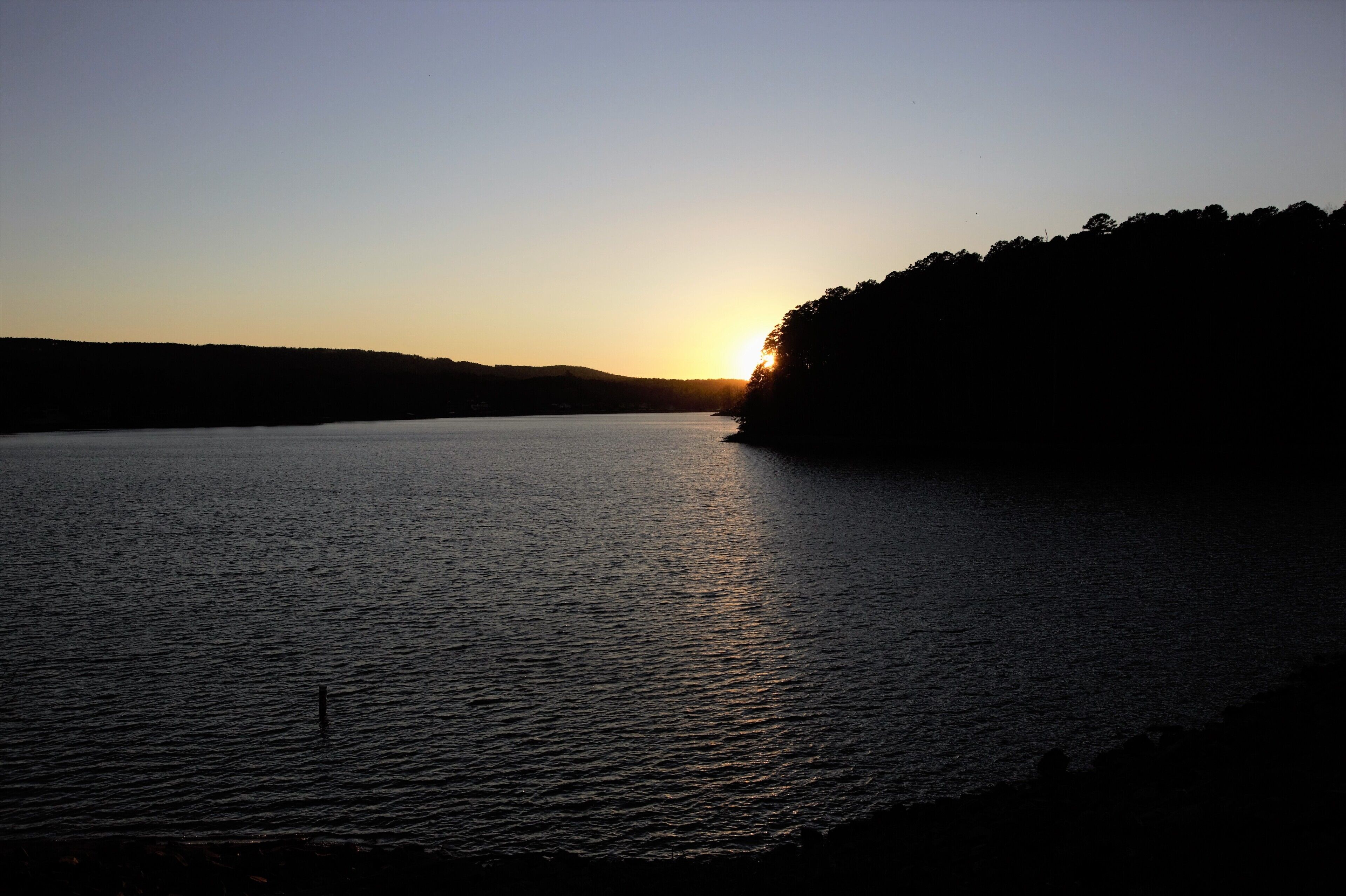 A calm lake at sunset with a forested shoreline.