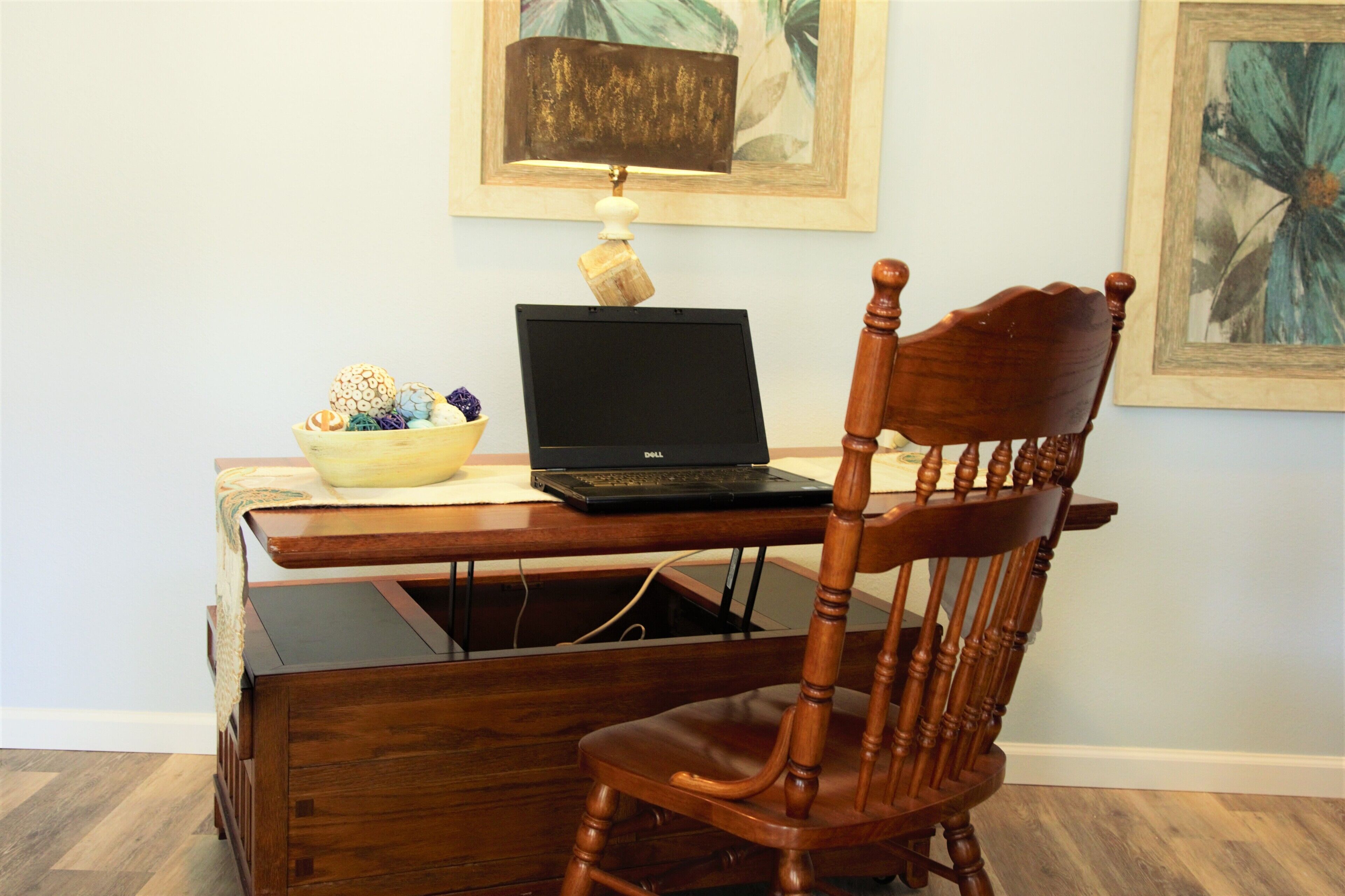 Un escritorio de madera con una laptop, un cuenco decorativo y una lámpara.
