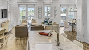 A spacious kitchen with a marble countertop, a sink, and a dining area with chairs and a table. - 'More Grayter' * Lake Views *  Walk To Beach * Gorgeous 5 BR Grayton Beach home * Neighborhood pool (Santa Rosa Beach)