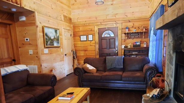 A wooden cabin interior with a sofa, armchair, and a fireplace. - Stay at Nina's Cabin in beautiful Blue Ridge, Ga "Gateway to the Smokeys" (Blue Ridge)