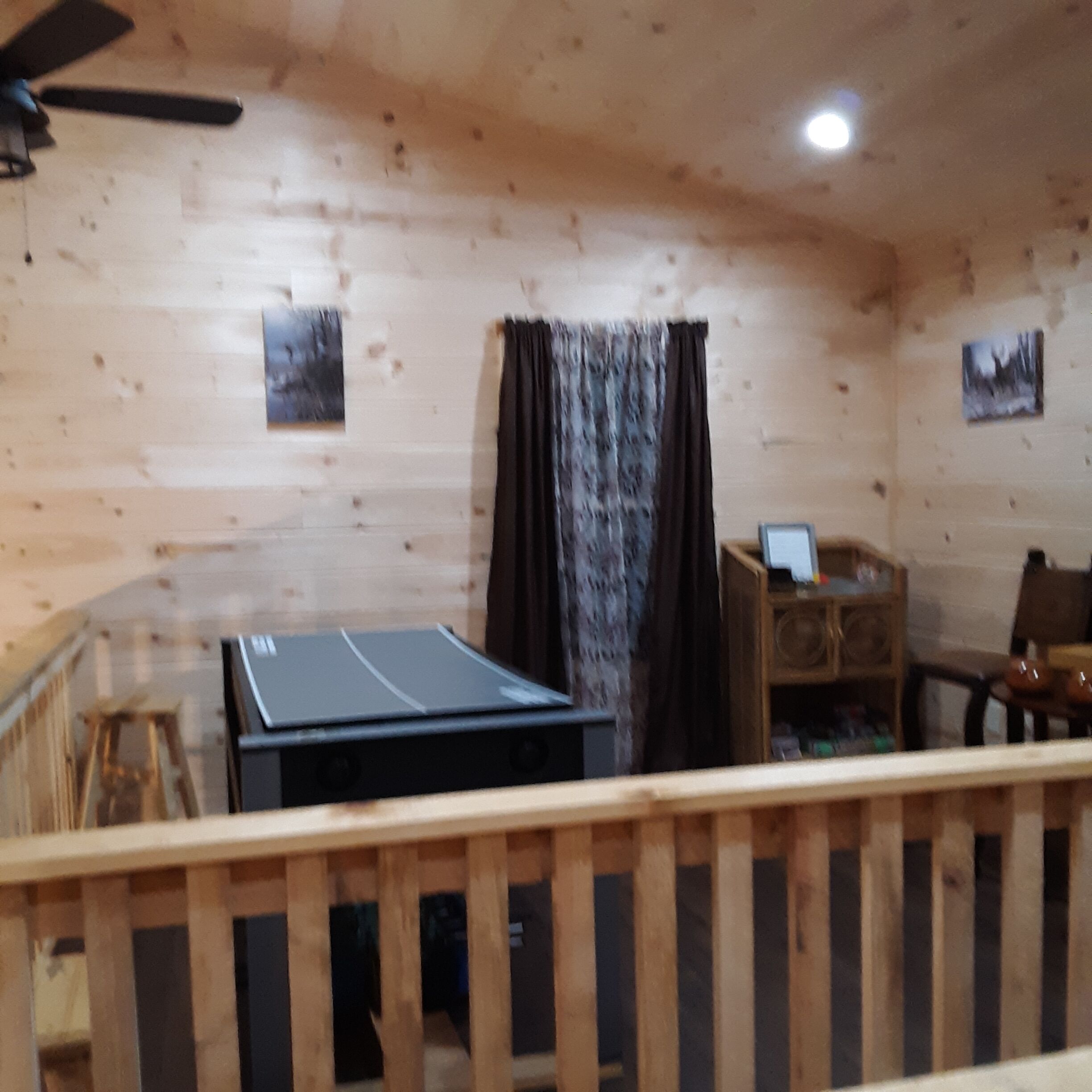 A room with a ping pong table, a desk with a computer, and a chair.