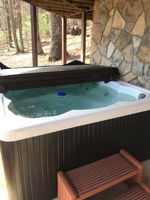 Relax in a serene hot tub surrounded by a natural wooded setting and a shaded seating area.