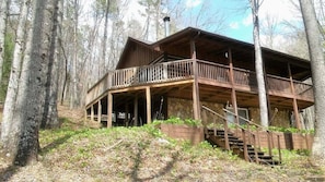 Relax on the upper-level balcony overlooking the forest, with a staircase leading to the cabin's entrance.