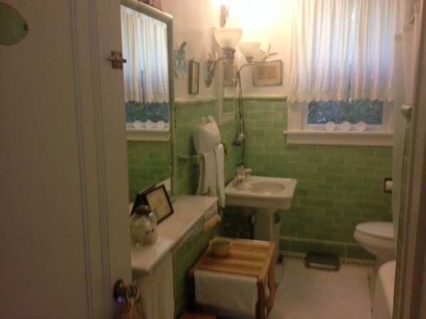 A bathroom with a green tiled wall, a white sink, a toilet, and a mirror above the sink.