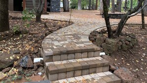 Una escalera de piedra conduce a un edificio de fachada pétrea, rodeado de árboles y zonas boscosas.