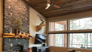 Un salón amplio con chimenea de piedra, una cabeza de ciervo montada en la pared y un gran ventanal con vistas al exterior.