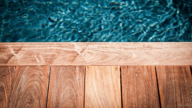 Borde de terraza de madera con una piscina al fondo.