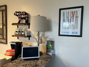 Eine Küchenarbeitsplatte mit einer digitalen Uhr, einer Lampe, einem Bilderrahmen mit Abbildungen von Skiern und einem Regal mit Gläsern und Behältern.