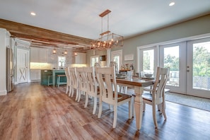 A spacious kitchen with a wooden ceiling, a dining area with white chairs, and a view of the outdoors through large sliding doors.