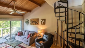 Una sala de estar con techo de madera, un sofá, un sillón de cuero, una mesa y una escalera de caracol.