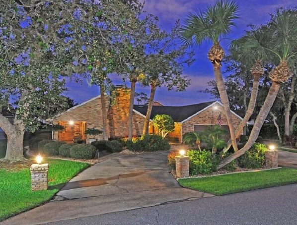 A brick house with a well-lit driveway and palm trees. - Pool side in Port Orange, Near beach, Gated Community, Bikers Welcome!Golf! (Port Orange)