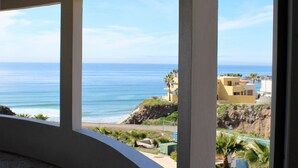 Una habitación con techo abovedado y ventanas amplias que ofrecen vistas al océano y edificios costeros.