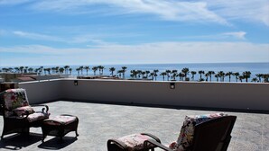 Una terraza en la azotea con dos sillones de mimbre y vistas al océano y palmeras.