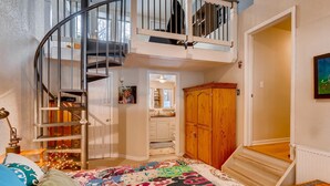 Une chambre à coucher avec un lit, une couverture colorée, une armoire en bois, un escalier en colimaçon et une vue sur la salle de bain.