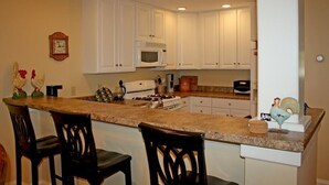 A kitchen with white cabinets, a microwave, a stove, and two bar stools. - Castle Hill Resort Condo (with on-site Aveda Spa) (cavendish)