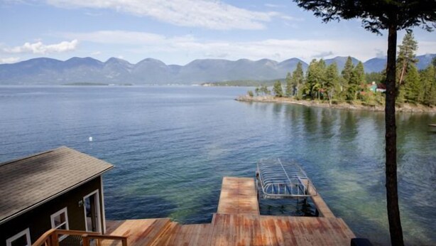 A wooden dock extending into a lake with a small cabin on the left and mountains in the background. - Lake House with Sauna, kayaks, S.U.P.'s, snorkeling sets and boat parking (Polson)